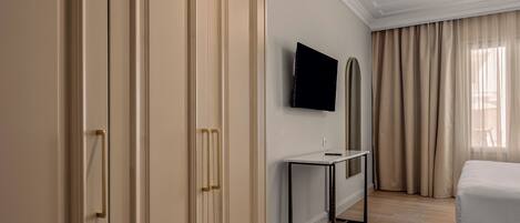 Habitación de hotel con una cama, televisión montada en la pared, escritorio y armario con espejo.