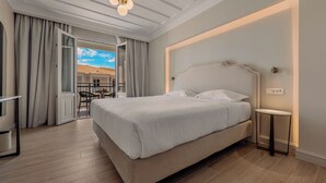 A bedroom with a bed, a bedside table, a chair, and a view through an open door. - Royal Nidri Suites (Nidri)