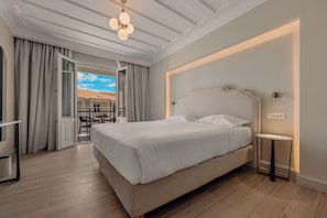 A bedroom with a bed, a bedside table, a chair, and a view through an open door. - Royal Nidri Suites (Nidri)