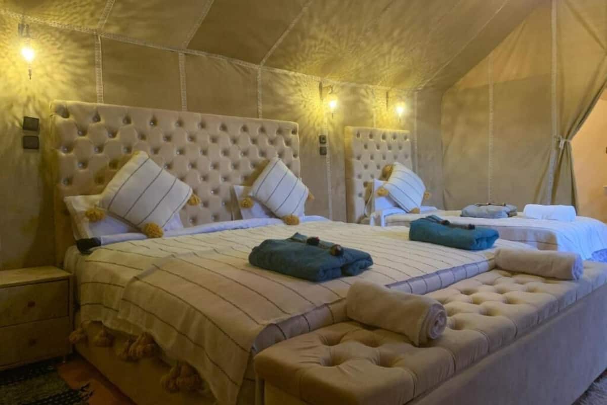 A tent-style room with two beds, each with a tufted headboard, and a bench at the foot of the beds.