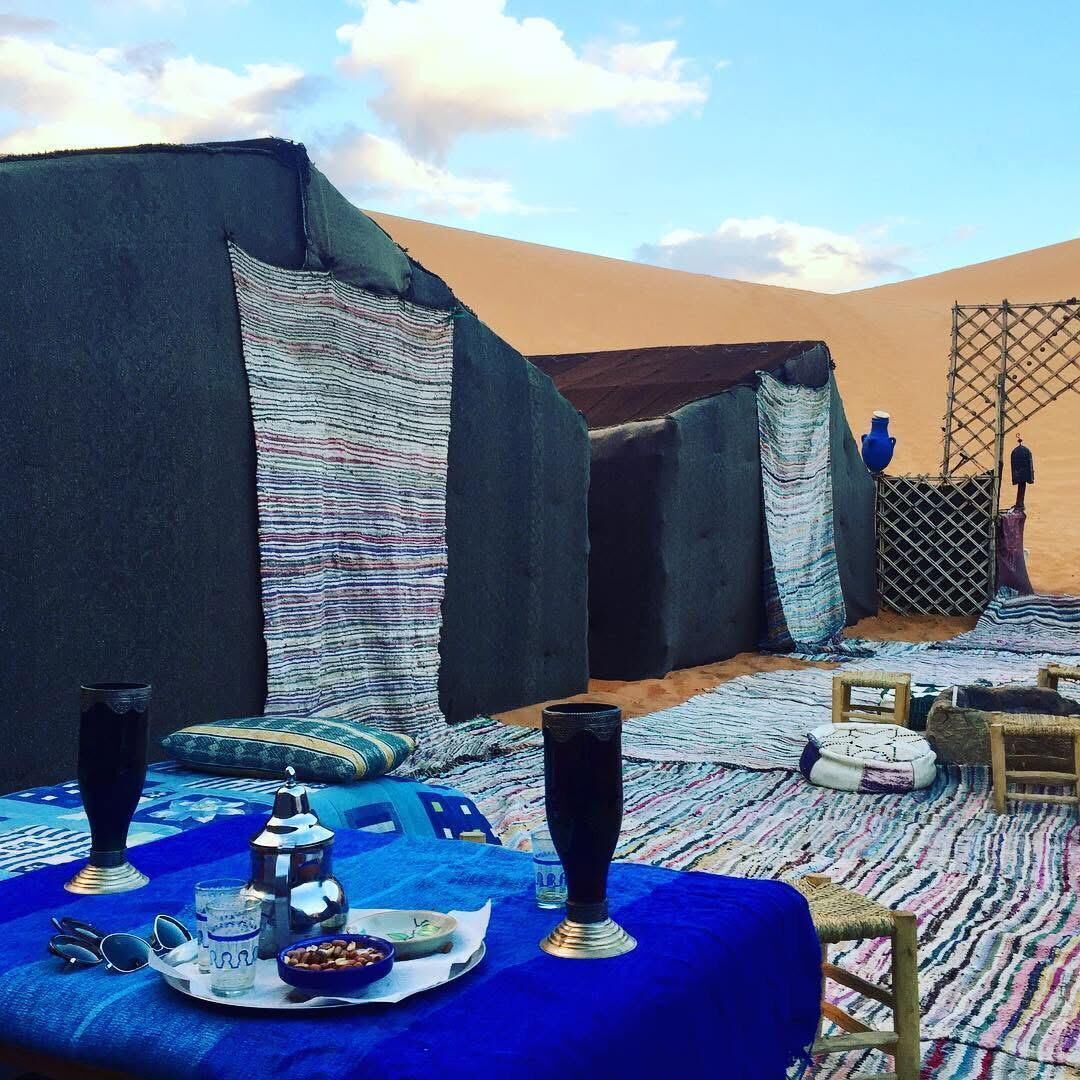 A desert tent with a table set for a meal, including glasses, a plate, and a bowl.