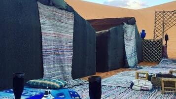 A desert tent with a table set for a meal, including glasses, a plate, and a bowl.
