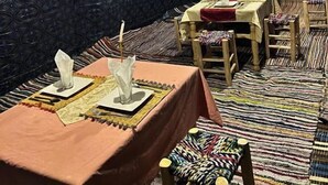 A room with patterned walls and ceiling, tables with white tablecloths and napkins, and wooden chairs. - Desert Camel Trekking Camp (Taouz)