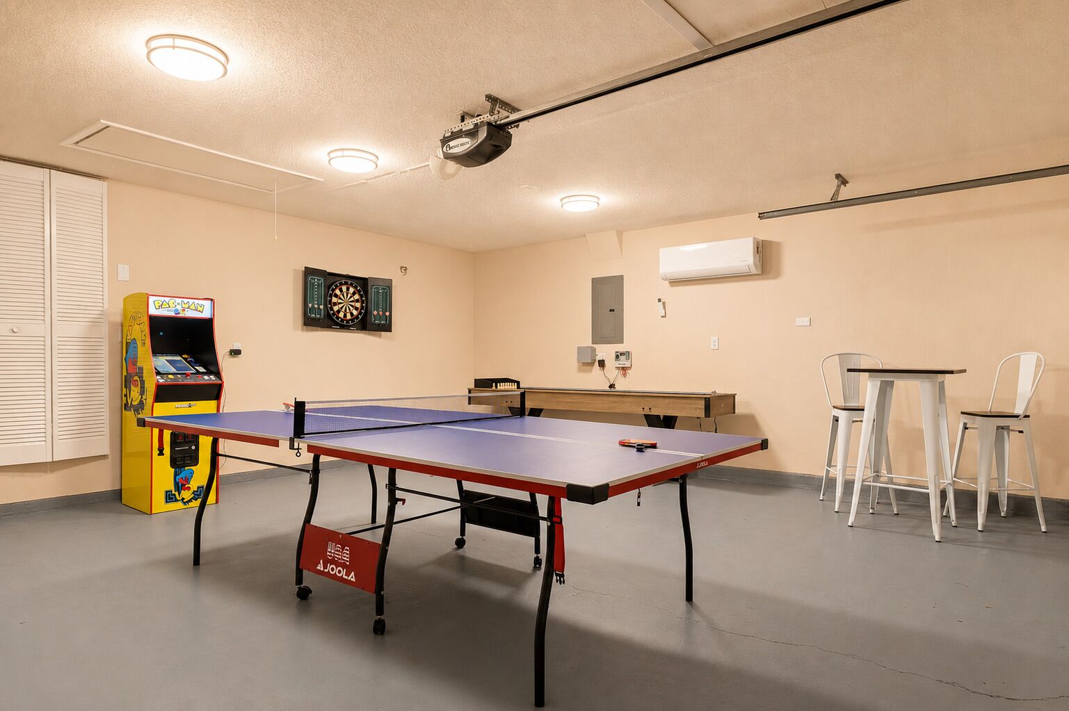 Ein Tischtennistisch mit Dartscheibe und einer Pac-Man-Spielmaschine in einem Raum mit an der Decke befestigtem Projektor.