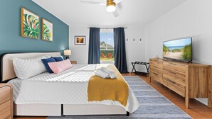 Un dormitorio moderno con cama, ventilador de techo, televisor y vistas al exterior.