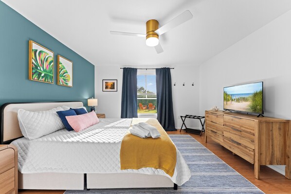 Camera da letto moderna con un letto, una ventola a soffitto, una televisione e vista sull'esterno.