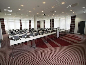 Una sala de conferències amb diverses taules, cadires i un sòl amb moqueta.
