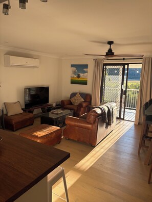 Een woonkamer met een televisie, leren banken, een eettafel en een balkon met uitzicht.