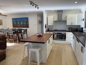 A modern kitchen with white cabinets, a wooden island, and a dining area with a painting.