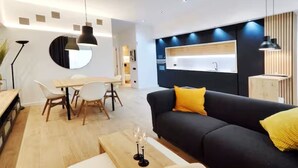 Ett modernt vardagsrum med en svart soffa, ett bord i trä som används som matbord och ett vitt soffbord.