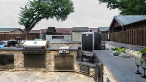 Une cuisine extérieure équipée d’un barbecue, d’un four encastré et d’un téléviseur.