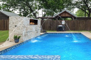 En swimmingpool med en stenvæg og bålsted, omgivet af et træhegn og træer.