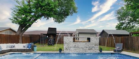 Ein Garten mit Swimmingpool, Steinmauer, Holzzaun und Baum.