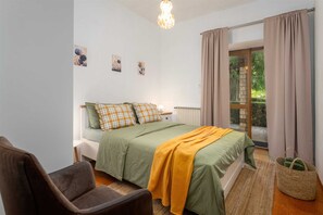 Ein Schlafzimmer mit einem Bett, einem Sessel, einem Fenster mit Vorhängen und Blick ins Grüne.