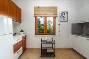 Eine Küche mit Holzausstattung, einer weißen Arbeitsplatte, einem Fenster mit Jalousien, einem Spülbecken und einem kleinen Wagen mit Aufbewahrungsbehältern.