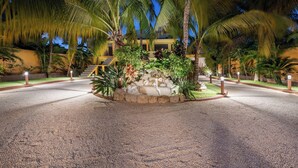 A well-lit outdoor area with palm trees, a stone fountain, and a building in the background. - Quinta Ixchel -3 Luxury Sac Bajo Beachfront Villas - Private Beach, Pool and... (Isla Mujeres)