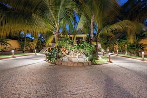 A well-lit outdoor area with palm trees, a stone fountain, and a building in the background. - Quinta Ixchel -3 Luxury Sac Bajo Beachfront Villas - Private Beach, Pool and... (Isla Mujeres)