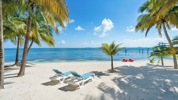 A beach with white sand, palm trees, and a clear blue sea. There are lounge chairs and a small boat. - Quinta Ixchel -3 Luxury Sac Bajo Beachfront Villas - Private Beach, Pool and... (Isla Mujeres)