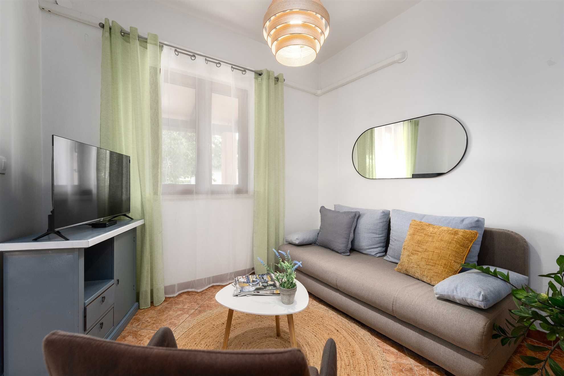 Un salon moderne avec un téléviseur à écran plat, un canapé avec des coussins, une table basse ronde et un miroir au mur.