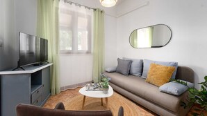 Ein modernes Wohnzimmer mit Flachbildfernseher, einer Couch mit Kissen, einem runden Couchtisch und einem Spiegel an der Wand.