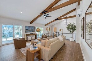 Ein großzügiges Wohnzimmer mit hohen Decken, Holzbalken, einem großen Sofa, einem Couchtisch und einem Essbereich.