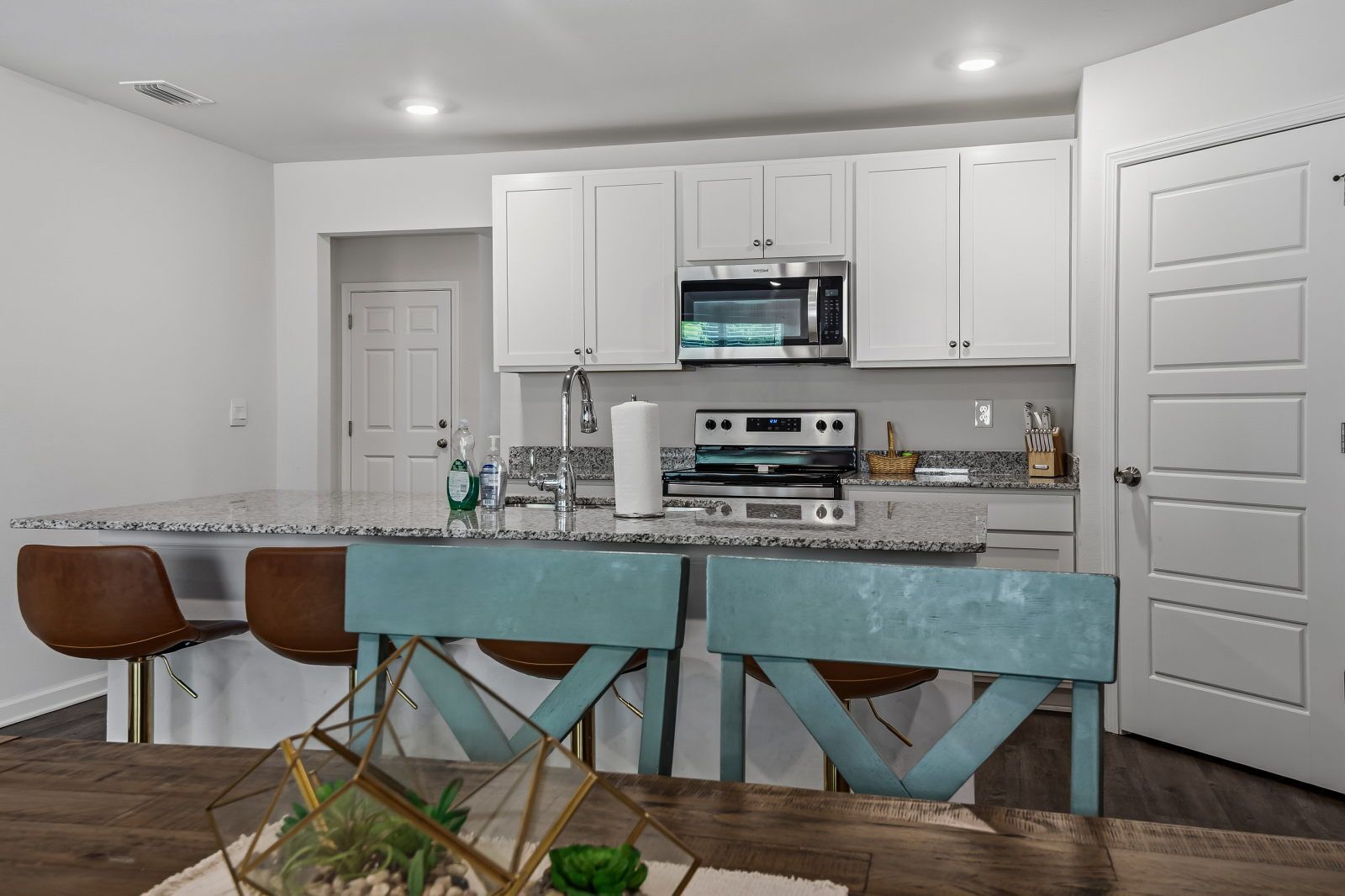 A modern kitchen with white cabinets, a built-in microwave, and a large island with bar stools.