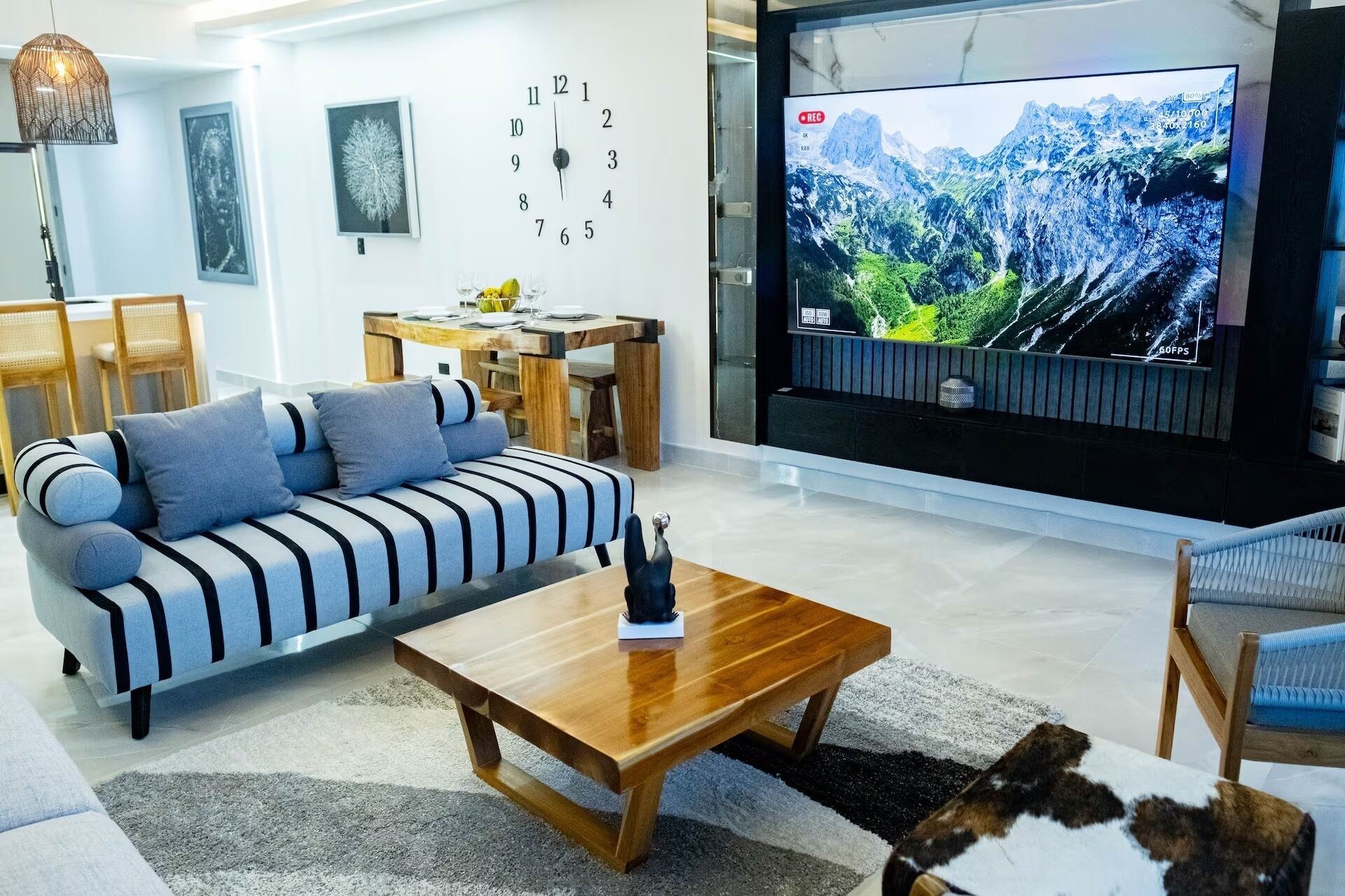 A modern living room with a sofa, coffee table, and a TV displaying a mountain landscape.
