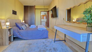 Une chambre à coucher avec un lit, une table de chevet, une lampe, une télévision et une plante.