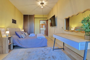 A bedroom with a bed, bedside table, lamp, TV, and a plant.