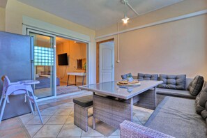 A living room with a glass-top table, a sofa, a baby high chair, and a television.