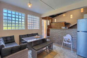 A modern kitchen with a built-in refrigerator, a dining area with a glass table and cushioned seating, and a small white high chair.