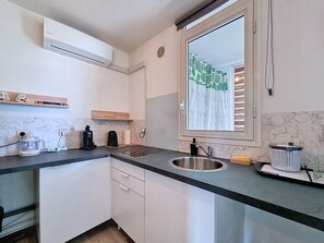 A compact kitchen with white cabinets, a marble backsplash, a built-in sink, and a window with a curtain. - Natur’Azur - AC - Sainte-Clotilde -Patio (Saint-Denis)