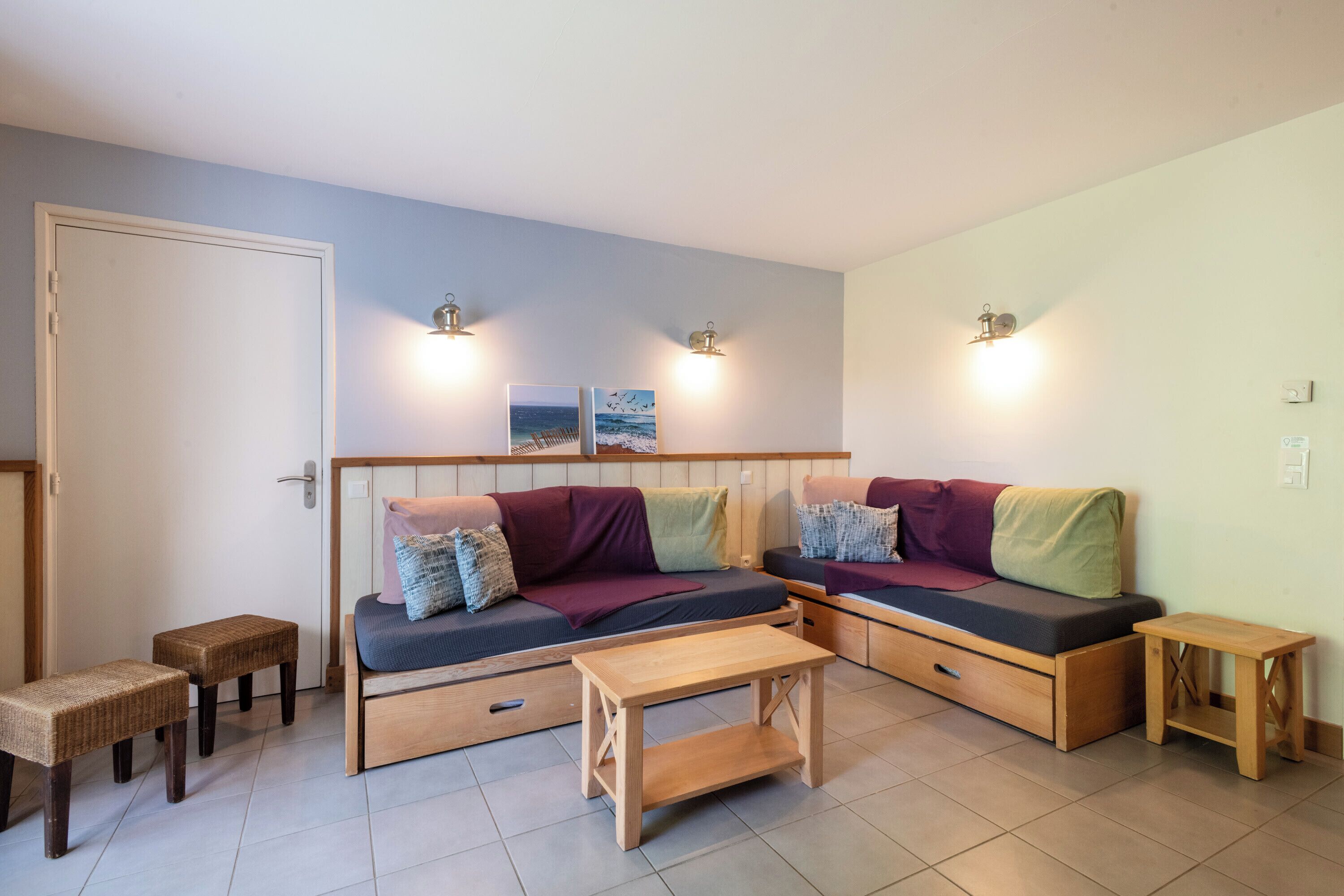 A compact living space with a sofa, two small tables, and wall-mounted lights.