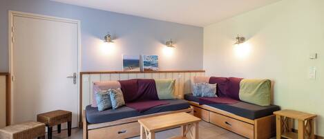 A compact living space with a sofa, two small tables, and wall-mounted lights.