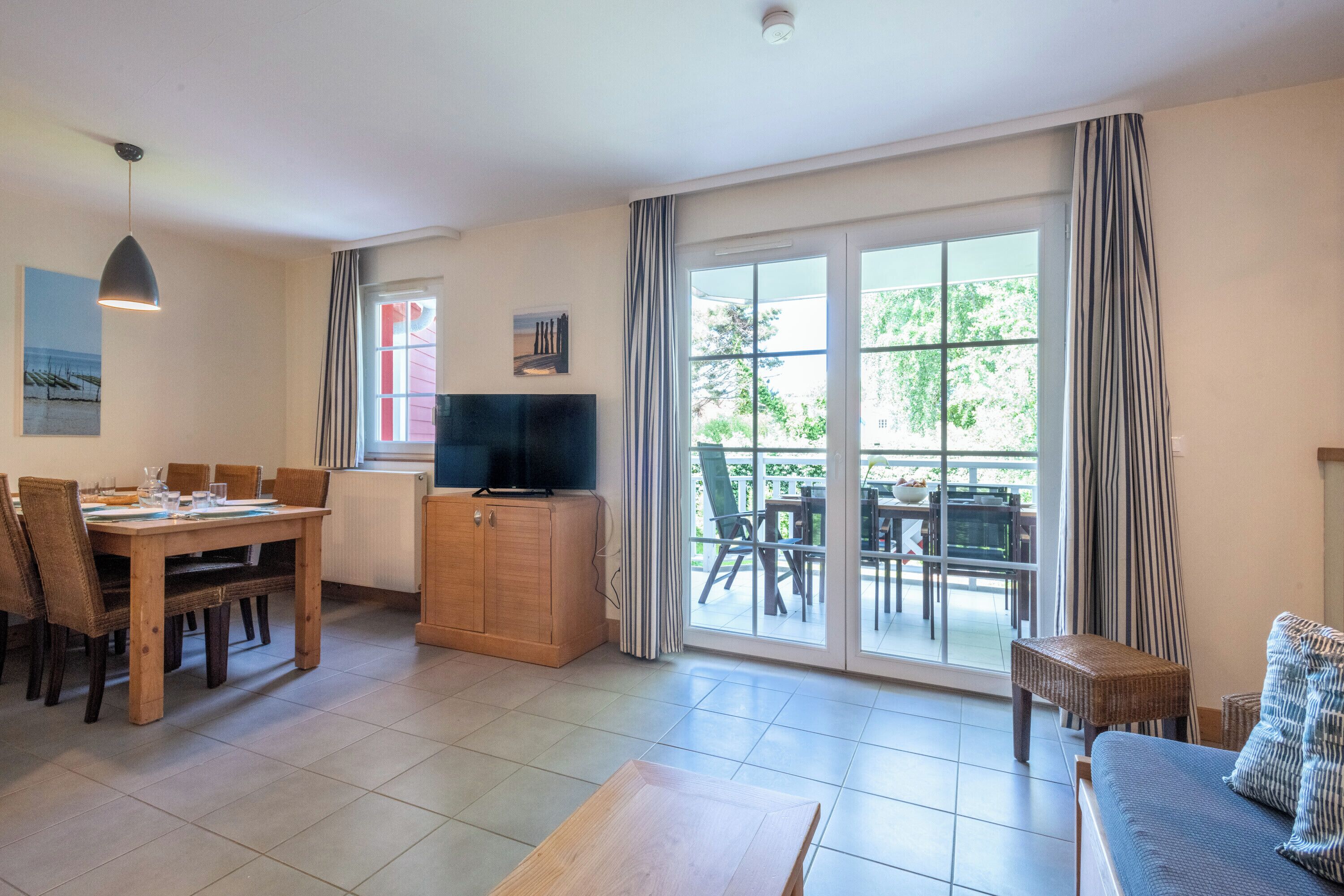 A spacious living area with a dining table, a sofa, a TV, and a sliding glass door leading to an outdoor patio.