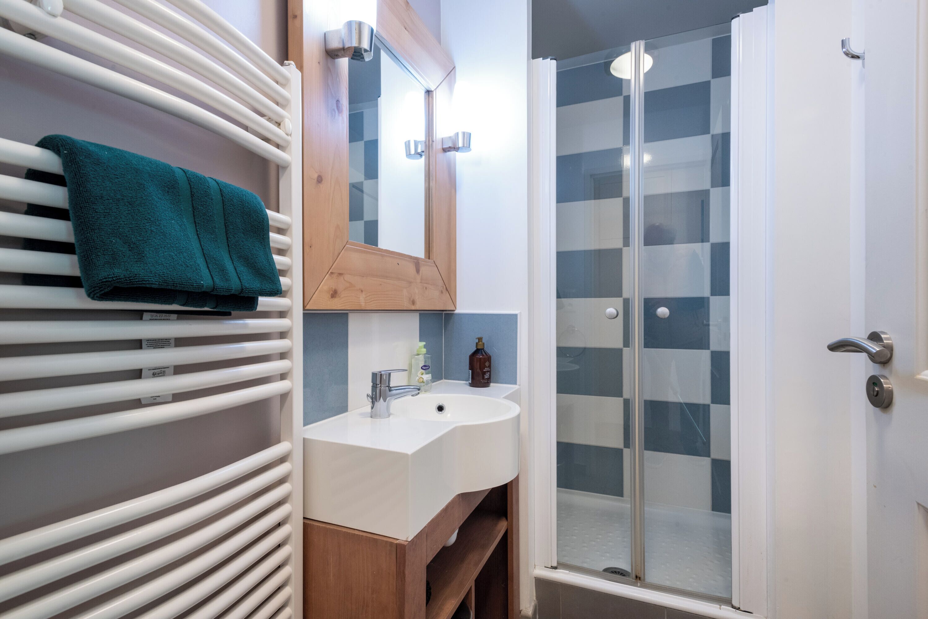 Une salle de bain avec un lavabo blanc, un miroir, un porte-serviettes et une douche dotée d’une porte en verre.