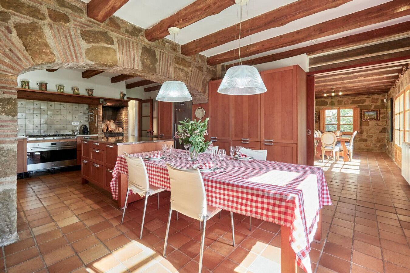Una cocina rústica con salpicadero de azulejos, vigas de madera y un comedor con mantel a cuadros.
