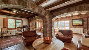 Ein rustikales Interieur mit Steinwänden, Holzbalken, Ledersofas und einem runden Holztisch.