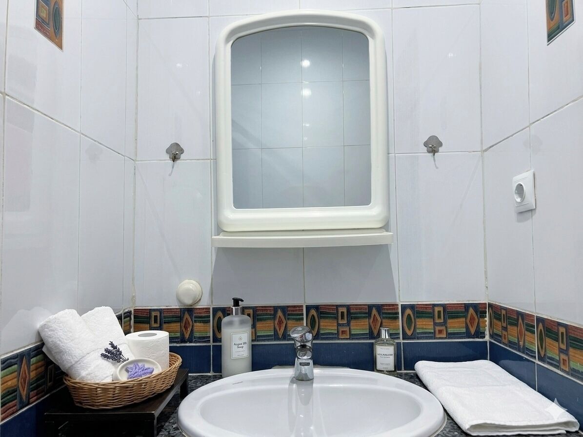 Ein Badezimmer mit Waschbecken, Spiegel, Handtuch und einem Korb mit Pflegeprodukten.