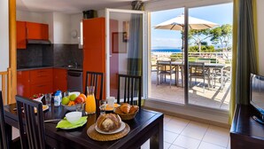 A dining area with a table set for breakfast, a kitchen with orange cabinets, and a balcony with outdoor seating. - Brusc Coastal Cabin Apartment for 6 (Six-Fours-les-Plages)