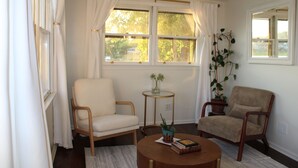 Una habitación con dos sillas, una mesita y un ventanal con cortinas.