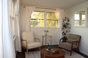 Quarto com duas cadeiras, uma mesa pequena e janela com cortinas.