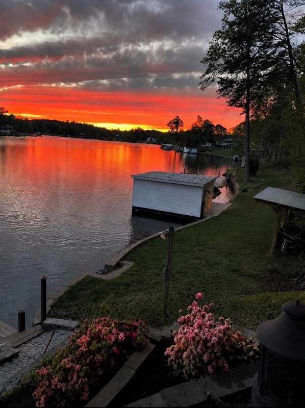 A lakeside view with a dock, a small shed, and a grassy area with pink flowers.