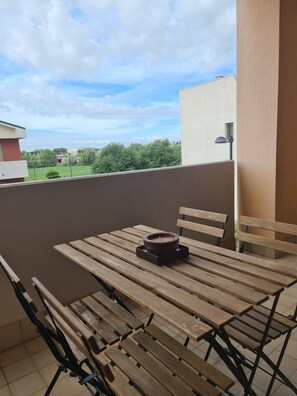 Ein Holztisch mit Stühlen auf einem Balkon, eine Kerze auf dem Tisch und im Hintergrund eine Ansicht von Gebäuden und Bäumen.