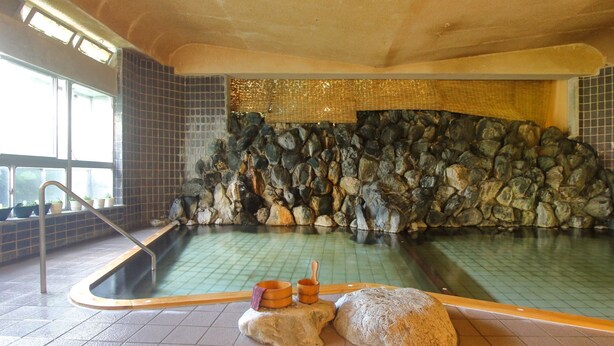 A hot spring bath with a stone wall backdrop, a wooden bench, and a metal ladder. - Nuruyu Onsen Sato Ryokan (Kurihara)