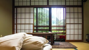 A traditional Japanese room with tatami flooring, a low table, a bed with white bedding, and a sliding door with a view of greenery. - Nuruyu Onsen Sato Ryokan (Kurihara)