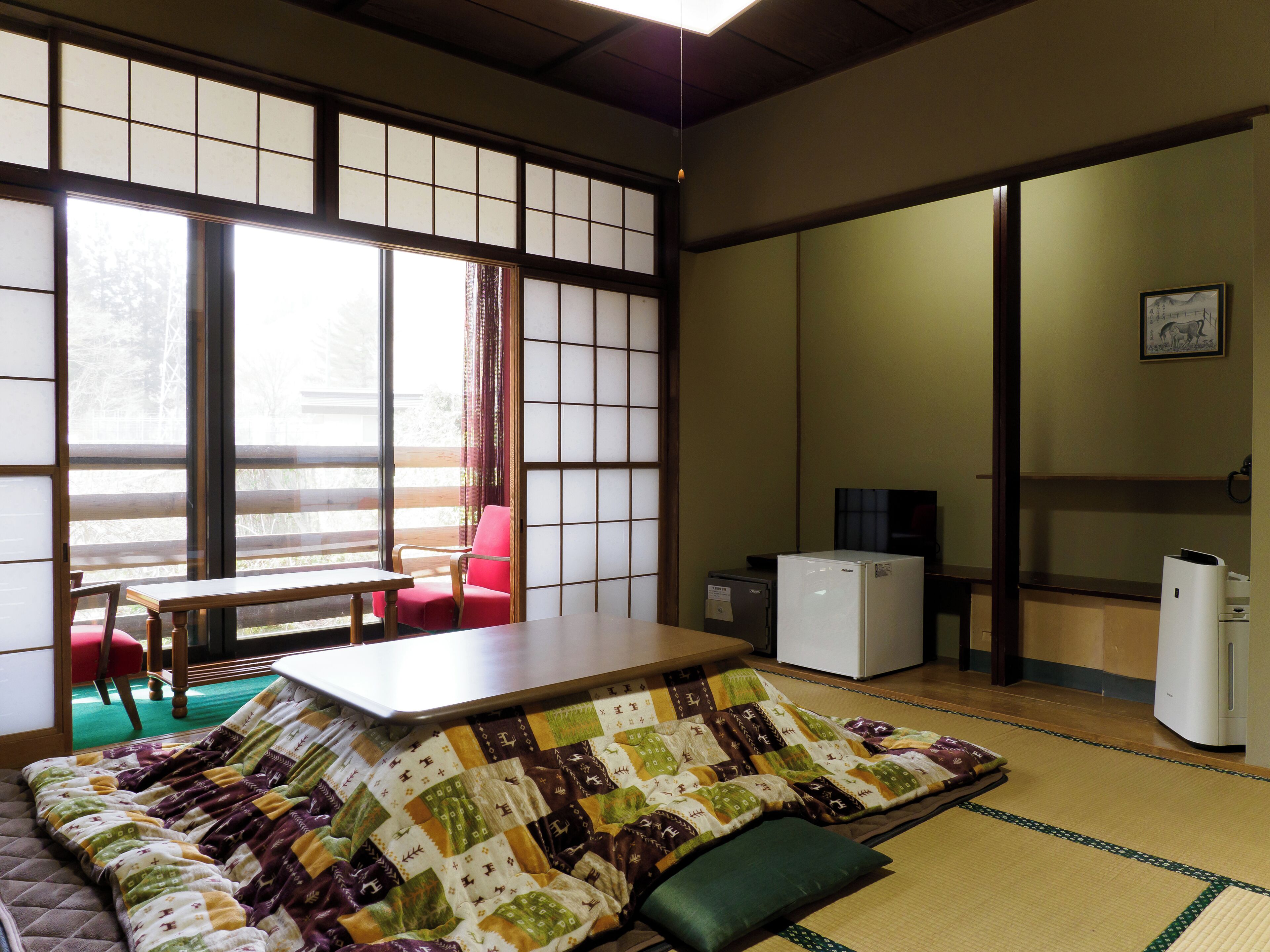 Ein traditioneller japanischer Raum mit Tatami-Boden, einem niedrigen Tisch, einem roten Sessel und einem weißen Kühlschrank.