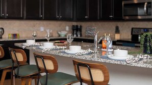 A modern kitchen with dark cabinets, a granite countertop, and a dining area with chairs and a table set for two. - 9 Themed Bedrooms, Pool & Jurassic Theater (Kissimmee)