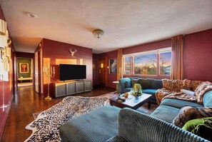 A living room with a television, sofas, a coffee table, and a large window. - Game Rooms, Hot Tub & Fire Pit (Arvada)