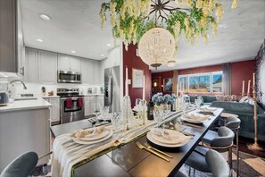 A modern kitchen with white cabinets, stainless steel appliances, and a dining area set for a meal. - Game Rooms, Hot Tub & Fire Pit (Arvada)